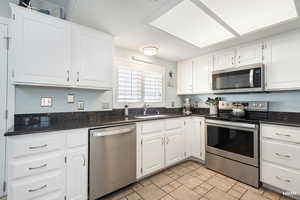 Kitchen with appliances with stainless steel finishes, white cabinets, and dark stone counters