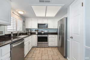Kitchen featuring appliances with stainless steel finishes, dark stone counters, white cabinets, pantry and tile flooring