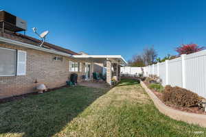 Fenced backyard lawn featuring a covered patio area and flower beds.