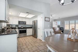 Kitchen with appliances with stainless steel finishes, white cabinetry, dark stone countertops, pantry, open floor plan, and tile flooring