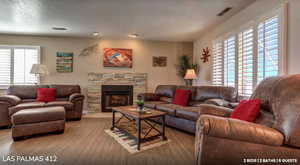 Living area featuring a stone fireplace, wood finished floors, and a textured ceiling