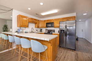 Kitchen with a peninsula, black appliances, a breakfast bar, dark wood-style floors, and brown cabinets