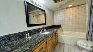Full bath with a textured wall, vanity, shower / bath combo, a textured ceiling, and light wood-type flooring