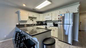 Kitchen featuring white appliances, a peninsula, dark stone countertops, a breakfast bar area, and light wood-type flooring