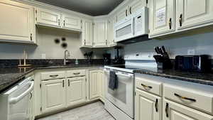 Kitchen with white appliances, white cabinetry, and dark stone counters