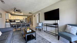 Living room with a textured ceiling, light wood-style flooring, and ceiling fan
