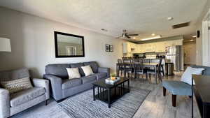 Living area with light wood-type flooring, a ceiling fan, and a textured ceiling