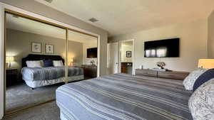 Carpeted bedroom featuring a textured ceiling, a closet, and ensuite bath