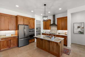 Kitchen with brown cabinets, appliances with stainless steel finishes, light stone counters, pendant lighting, and a kitchen island with sink