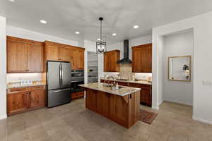 Kitchen with brown cabinetry, stainless steel appliances, light stone countertops, a breakfast bar area, and a kitchen island with sink