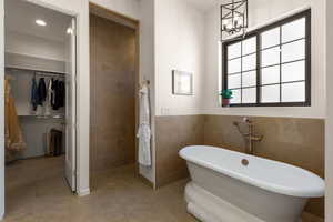 Bathroom with a freestanding bath, a walk in closet, tile walls, a chandelier, and light tile patterned floors