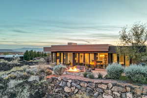 Back of property at dusk featuring a patio, stucco siding, and an outdoor living space with a fire pit