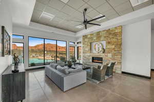 Living area with ceiling fan, concrete flooring, a stone fireplace, a raised ceiling, and a drop ceiling