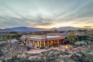 Back of house at dusk featuring a mountain view, stucco siding, a fire pit, and a patio area