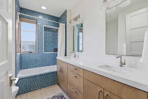 Full bathroom featuring tiled shower / bath combo, double vanity, and light tile patterned floors