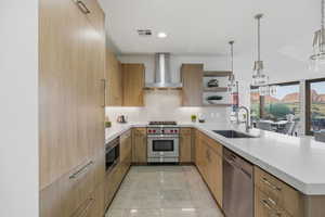 Kitchen featuring modern cabinets, open shelves, appliances with stainless steel finishes, wall chimney exhaust hood, and light stone counters