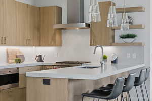 Kitchen featuring wall chimney exhaust hood, modern cabinets, light stone countertops, and pendant lighting
