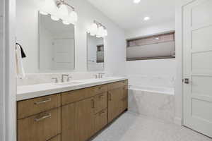 Bathroom featuring a garden tub, double vanity, and dark speckled floor