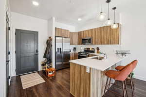 Kitchen featuring brown cabinets, stainless steel appliances, hanging light fixtures, a kitchen breakfast bar, and a peninsula