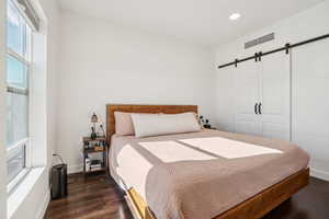 Bedroom with a barn door and dark wood-style floors