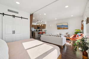Bedroom with a barn door, dark wood finished floors, recessed lighting, and freestanding refrigerator