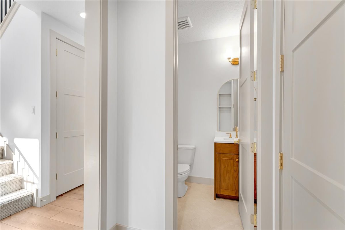 Hallway leading to a half bath with a wood-finish vanity and gold-tone hardware, white paneled doors, and light wood-finish flooring
