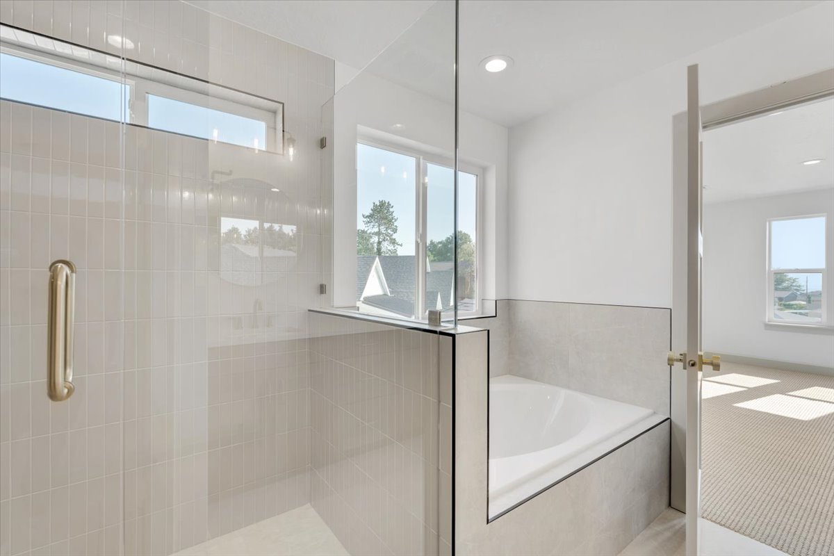 Contemporary bathroom featuring a frameless glass shower enclosure, a built-in soaking tub, large format tile surrounding the tub, and sleek light-colored wall tile in the shower