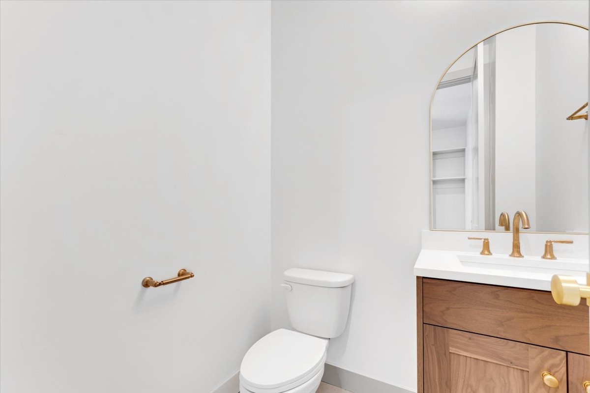 Bathroom vanity featuring a wood-finish cabinet, white countertop, gold-tone hardware, and an arched mirror