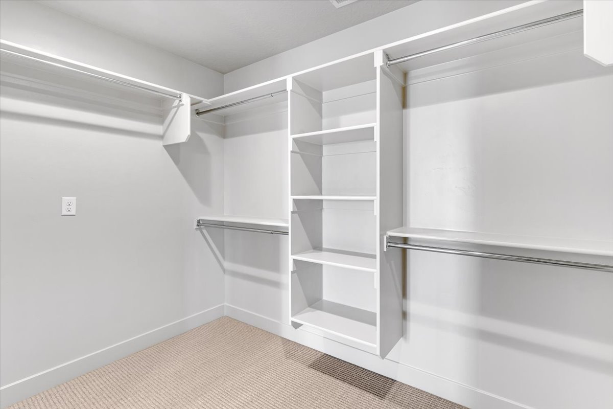 Walk-in closet featuring built-in shelving, multiple hanging rods, white trim, and light-colored carpeting