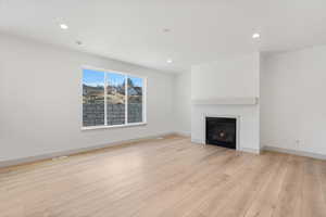 Unfurnished living room featuring light wood-type flooring, a glass covered fireplace, and recessed lighting