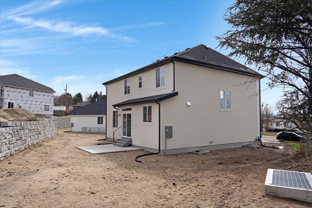 Rear exterior featuring stucco siding, a black shingle roof, and a concrete patio