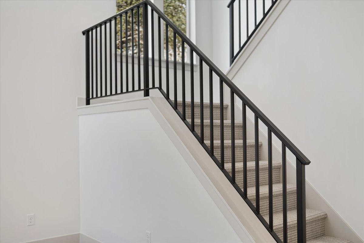 Staircase featuring black metal balusters, a black metal handrail, and carpeted treads