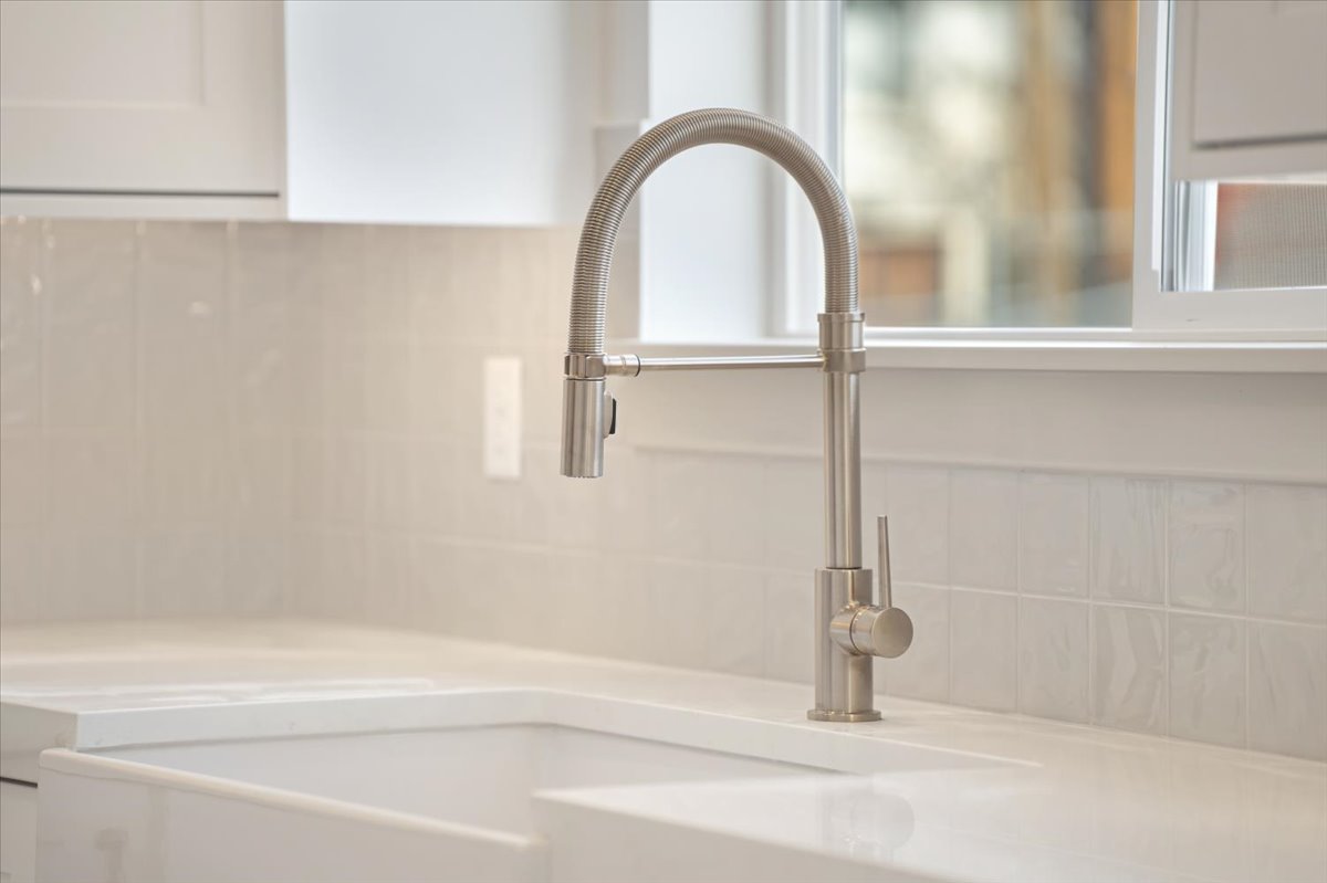 Brushed nickel pull-down faucet with a white farmhouse-style sink, solid surface countertop, and subway tile backsplash