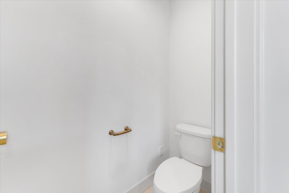 Compact powder room featuring a white toilet, bright white walls, and a light-toned baseboard