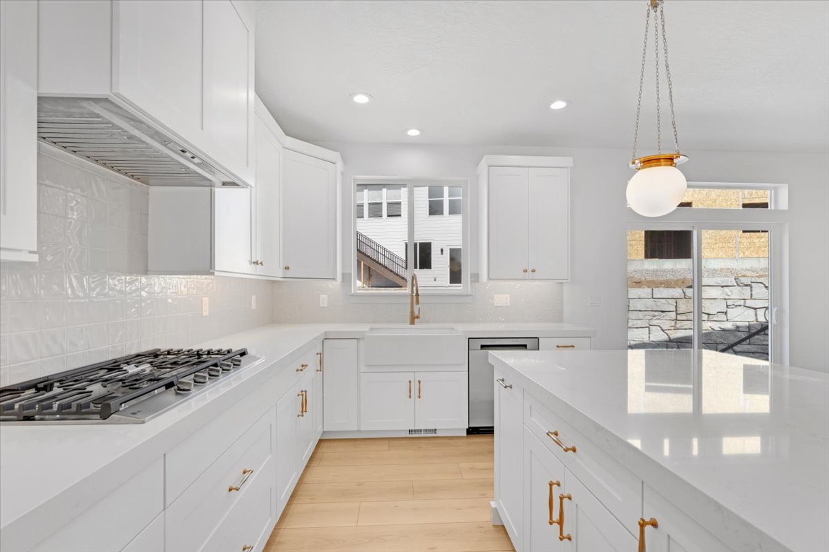Contemporary kitchen featuring white cabinetry, light countertops, gold-tone hardware, a stainless steel gas range, and wood-finish flooring