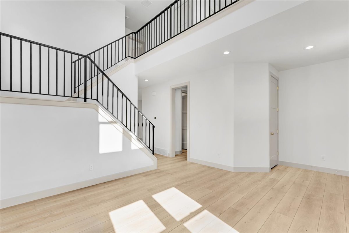 Two-story entryway featuring wood-finish flooring, a contemporary staircase with black metal railings, recessed lighting, and crisp white walls