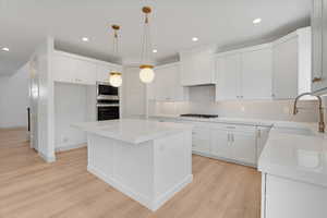 Kitchen with white cabinets, light wood-style flooring, a center island, and stainless steel appliances