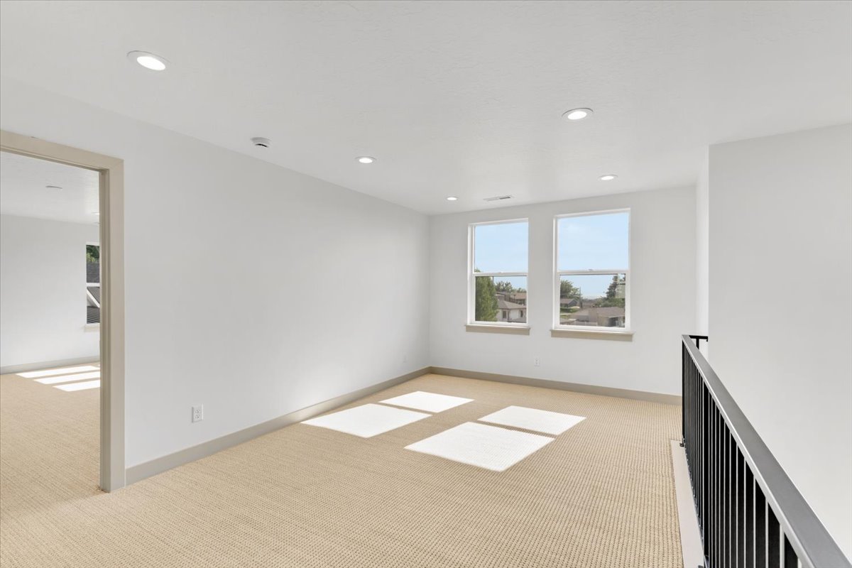 Carpeted upper-level landing with recessed lighting, two windows, and a black metal railing