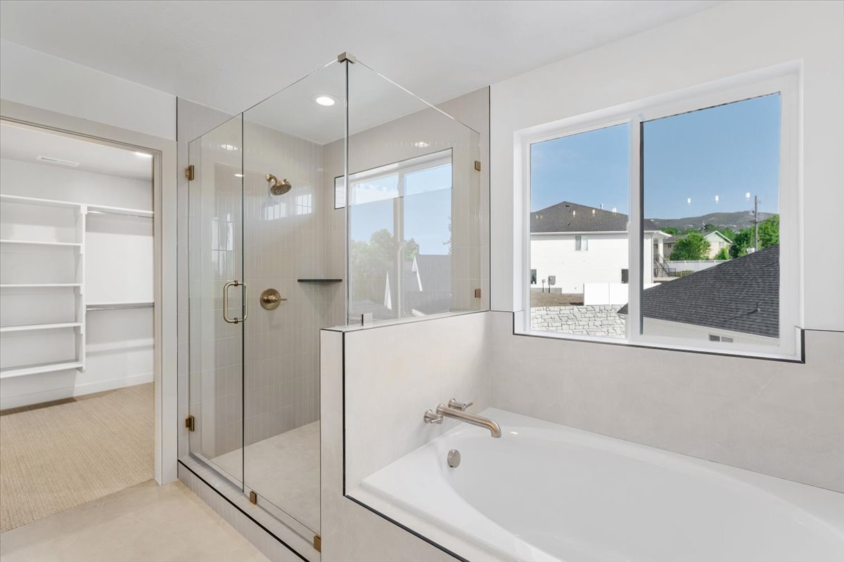 Spacious bathroom featuring a glass-enclosed shower with brass fixtures, a built-in bathtub with a deck-mounted faucet, and an expansive window