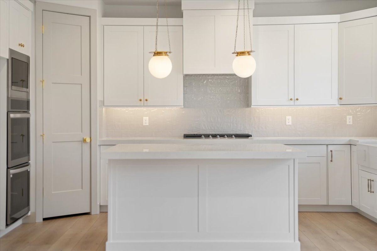 Modern kitchen featuring a central island with a solid surface countertop, white shaker-style cabinetry with gold hardware, a textured subway tile backsplash, and wood-finish flooring