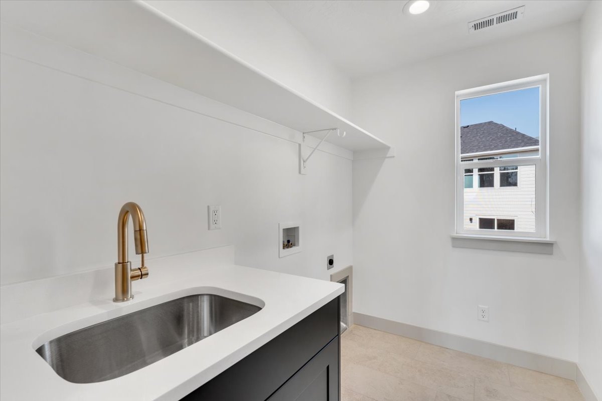 Utility space featuring a stainless steel sink, bronze-finish faucet, white countertop, and dark cabinetry