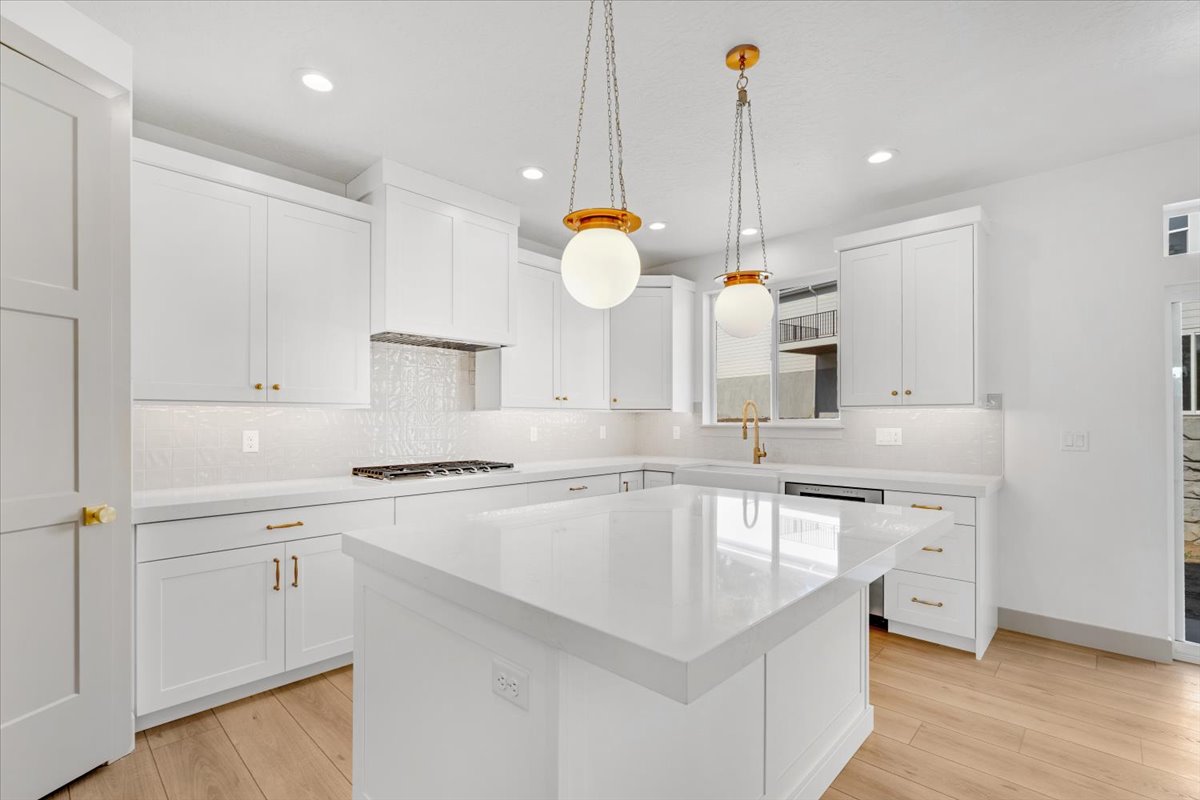 Modern kitchen featuring white shaker cabinetry, an expansive center island with a stone countertop, a tile backsplash, and wood-finish flooring