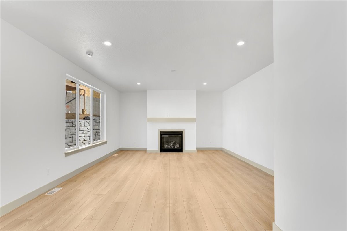 Expansive room featuring light wood-finish flooring, a contemporary fireplace with a light-colored mantel, recessed lighting, and a large window with white trim