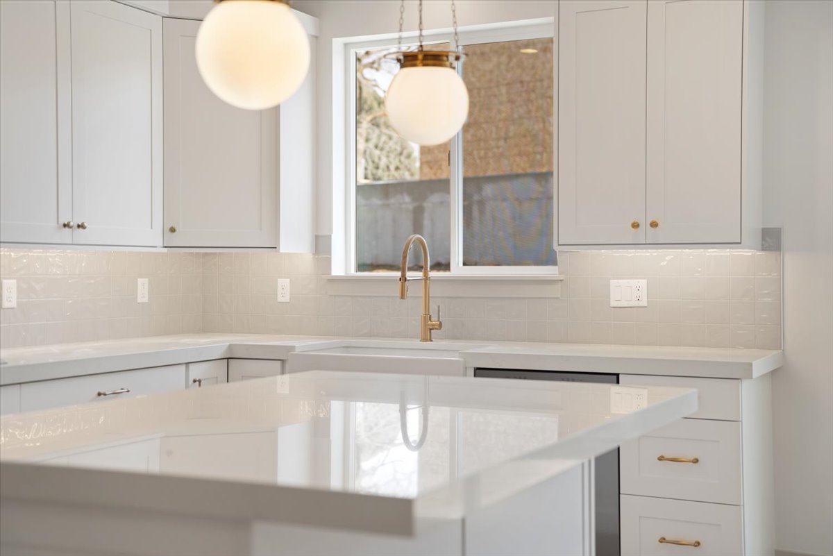 Kitchen featuring white shaker cabinetry, light countertops, a kitchen island, brass-toned fixtures, and under-cabinet lighting