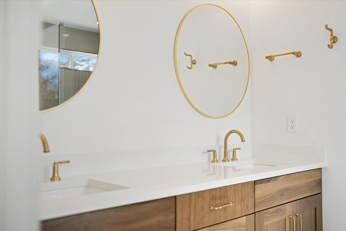 Dual vanity with brass fixtures, integrated sinks, white countertops, and wood-finish cabinetry