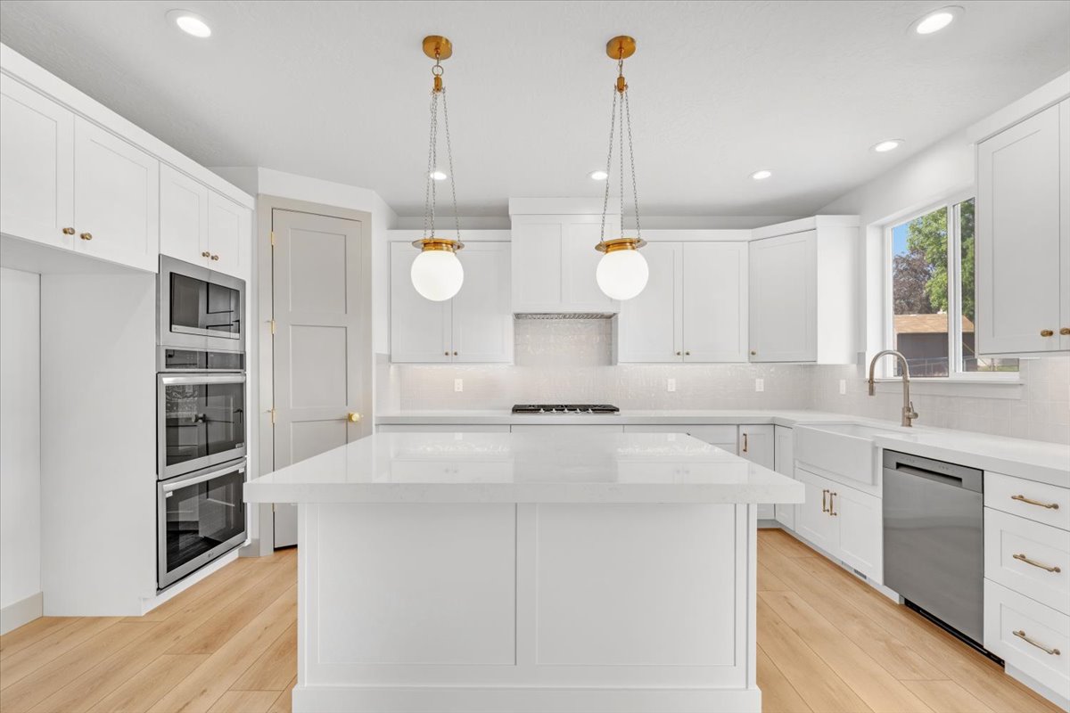 Modern kitchen with a central island, white cabinetry, integrated stainless steel appliances, and wood-finish flooring