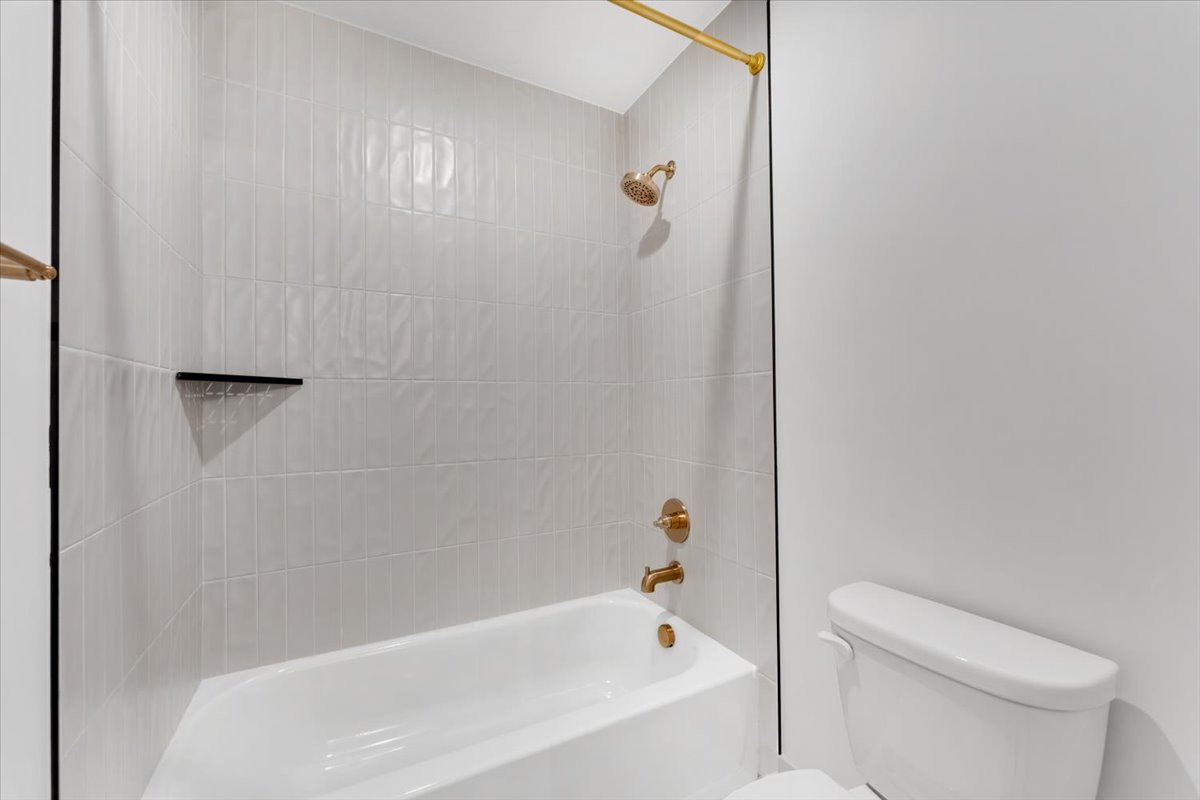 Bathroom featuring a white bathtub, white tile surround with a built-in black shelf, and gold-finish fixtures