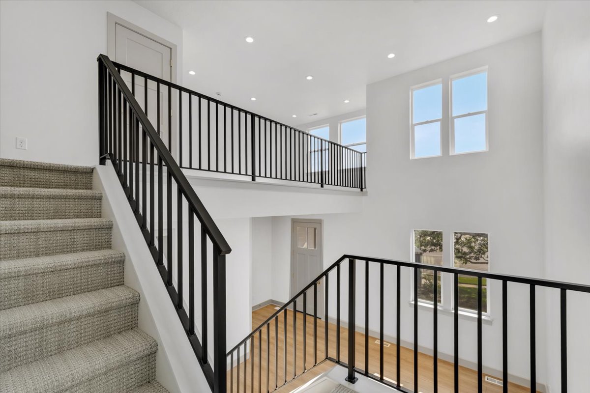 Two-story foyer featuring a carpeted staircase with contemporary black iron balusters, recessed lighting, and multiple windows providing ambient light