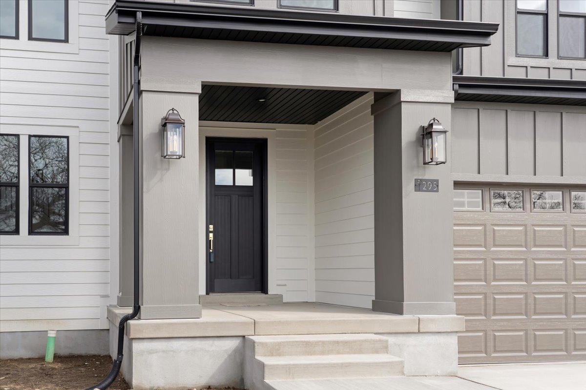 Modern residential exterior featuring a covered entry, dark paneled front door with upper lites, two bronze-finish wall lanterns, light gray horizontal siding, and an attached garage with a paneled door