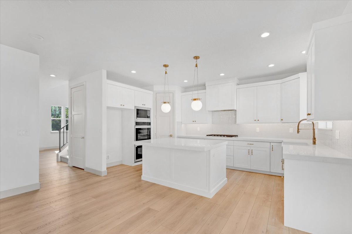 Bright kitchen featuring a central island, light wood-finish flooring, white cabinetry, quartz countertops, and modern pendant lighting